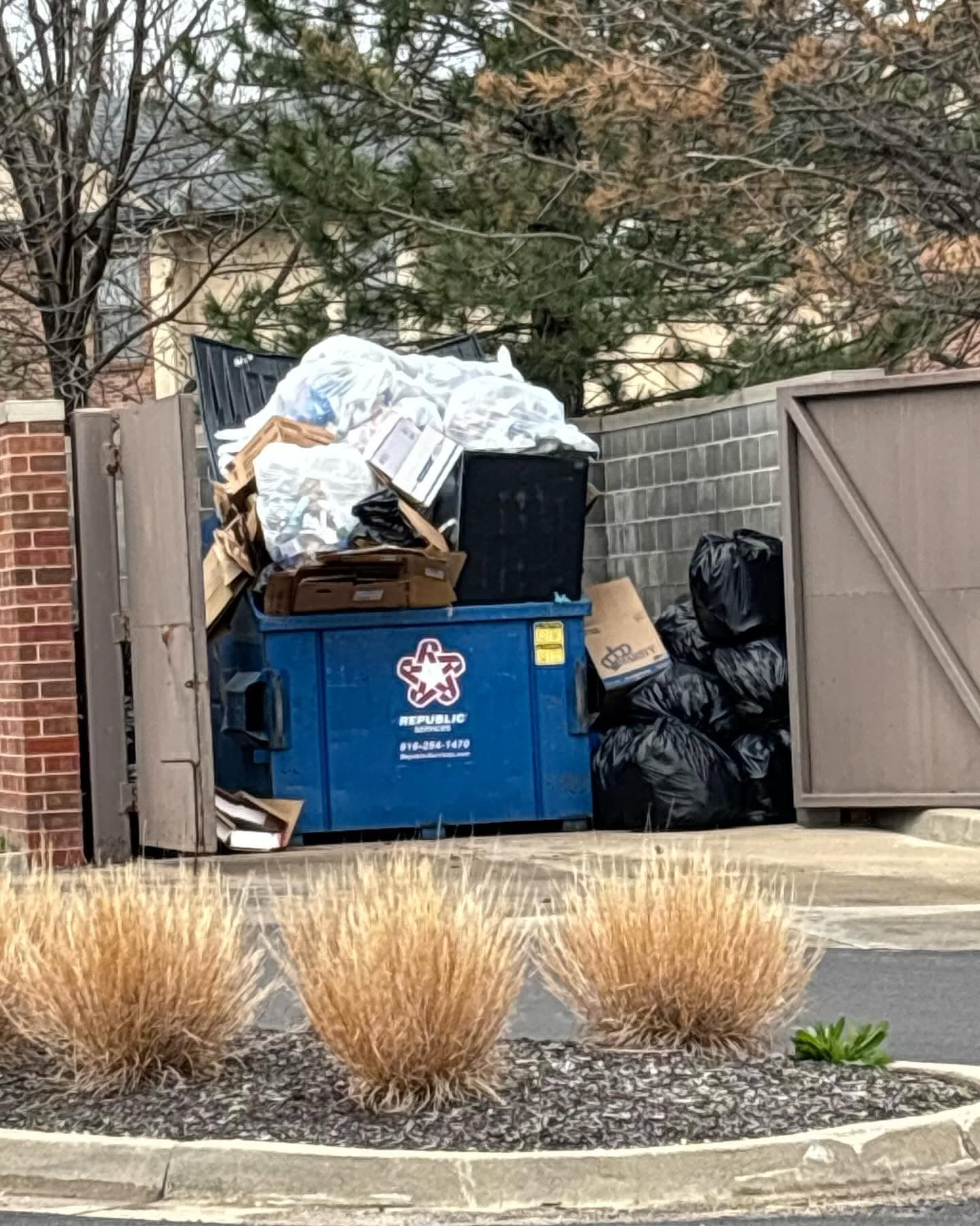 Dumpster corral overflow with furniture and trash.